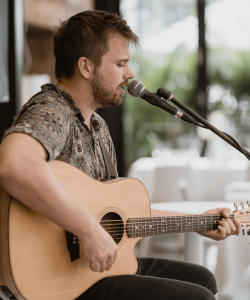 male guitarist vocalist sitting on a chair singing