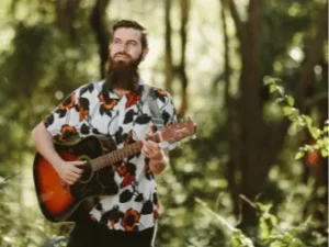 Brandon Duff playing acoustic guitar in a forest