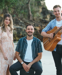 Maple Vale Trio posing on a beach with acoustic guitar