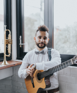 Dom Diaz with acoustic guitar beside a trumpet