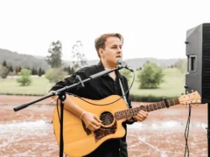 Jamieson Postle singing with acoustic guitar at an outdoor wedding