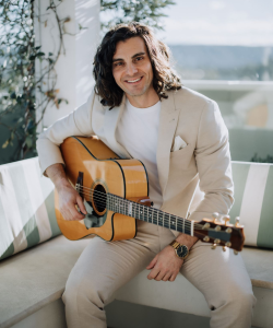 Luke Michael in a cream suit playing acoustic guitar