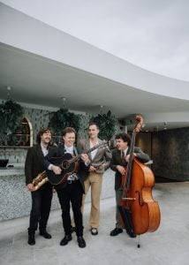 Pick and The Pockets quartet with saxophone, guitar, drumsticks and double bass in a full-length group portrait.